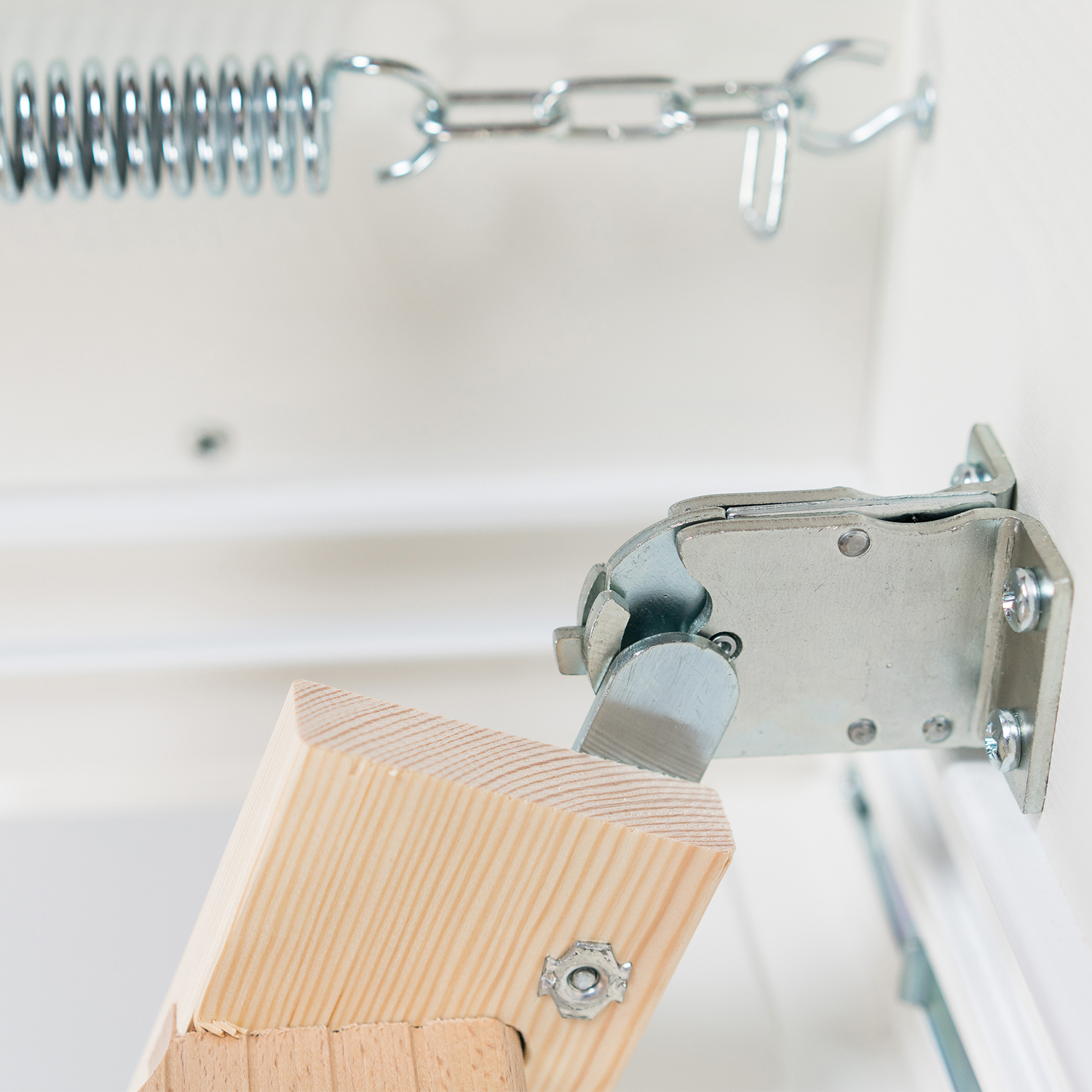 Close-up of a metal latch and spring mechanism attached to a wooden loft ladder.